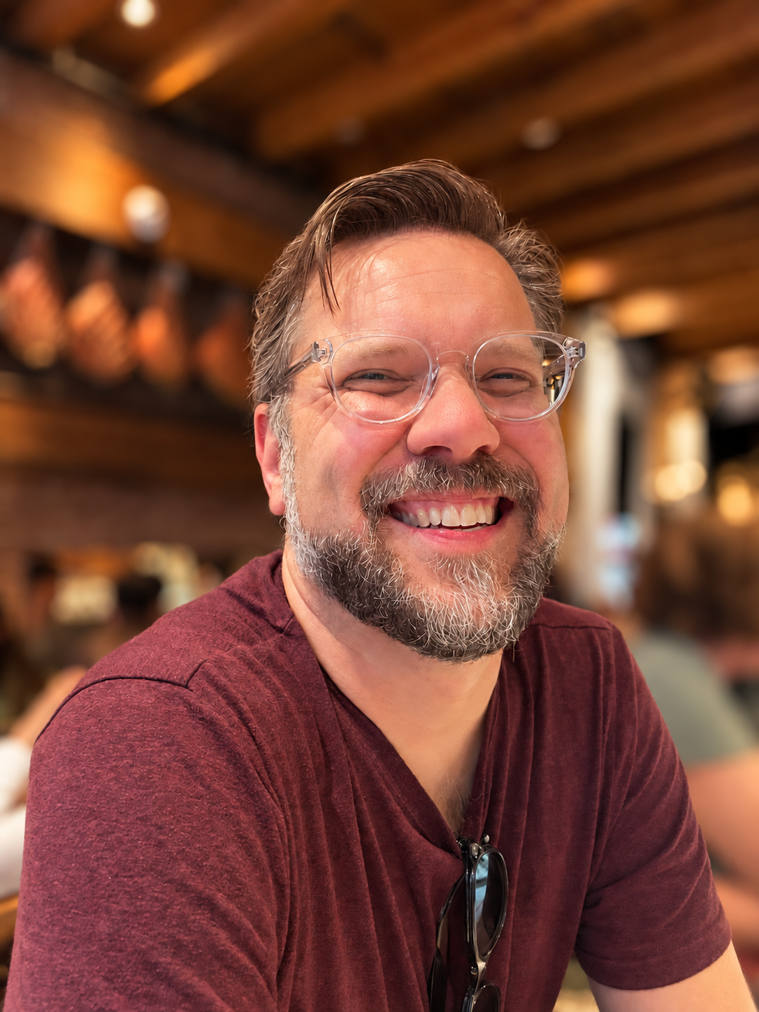 Jason smiling in a café, wearing glasses and a burgundy shirt.